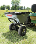 Tow Behind Broadcast Spreader With 75 Pound Capacity For Semi Commercial Lawn Care attached to a green tractor in a field