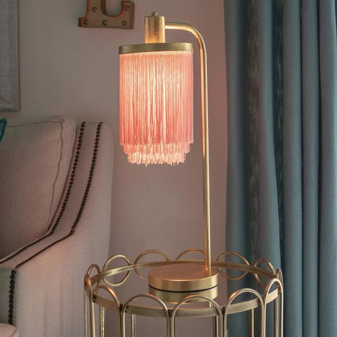 Framboise Fringe Shade Table Lamp With Gold Leaf Finish on a side table in a living room setting with pink tassel