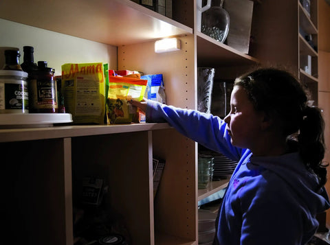 Child picking snacks lit by Wireless Motion Sensing LED Night Lights Six Pack Tiny Stick Anywhere White Battery Powered Auto On When Motion Is Detected In Darkness Great For Hallways Closets And Stairs.