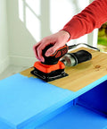 Person using a Quarter Sheet Orbital Palm Sander Professional Grade 220 Watt Motor Featuring A Snappy Pressure Trigger Switch Lightweight Orange Body for sanding wood.