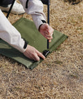 Person setting up Ultra Lightweight Outdoor Camping Backrest Chair With Carry Bag For Park Vibes And Beach Days on grass.