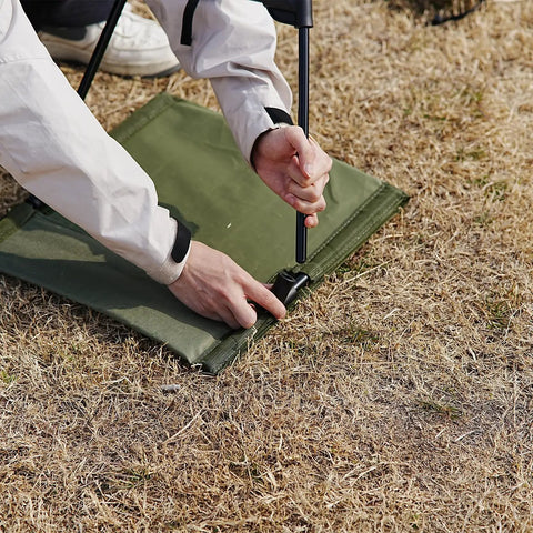 Person setting up Ultra Lightweight Outdoor Camping Backrest Chair With Carry Bag For Park Vibes And Beach Days on grass.