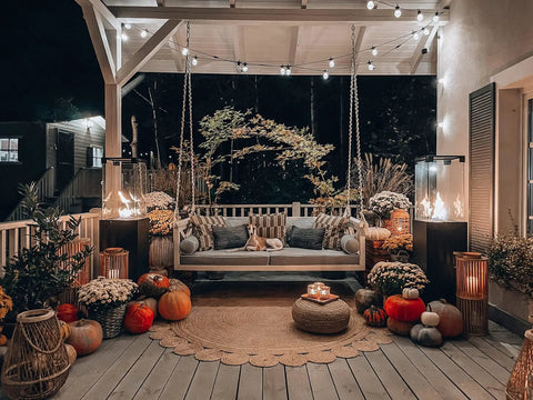 Outdoor patio with hanging swing, decorated with pumpkins and illuminated by smokeless 360 degree propane patio heater towers at night.