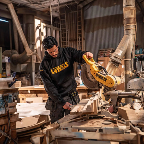 Man in workshop wearing Men's Carrier Hoodie Black Pullover Sweatshirt with Front Pockets, using saw for woodworking.