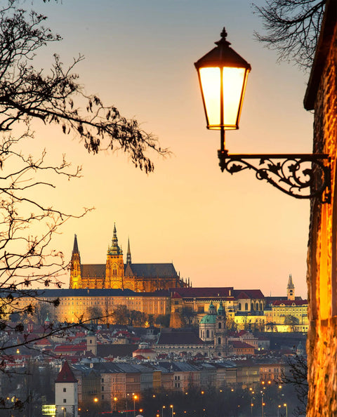 I don't know who the person in the image is, but they are standing on a wall with a lamp post overlooking a city at sunset.