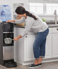 Person using a top loading water dispenser with hot and cold water, 5 gallon bottle compatible, pet drinking station, in kitchen
