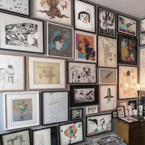 Gallery wall with various framed artworks in different styles and sizes displayed in a cozy room with warm lighting.