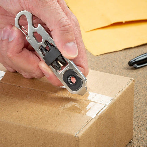 Hand using DoohicKey Ratchet Key Tool Keychain Friendly Pocket Multitool With Carabiner Clip on cardboard box