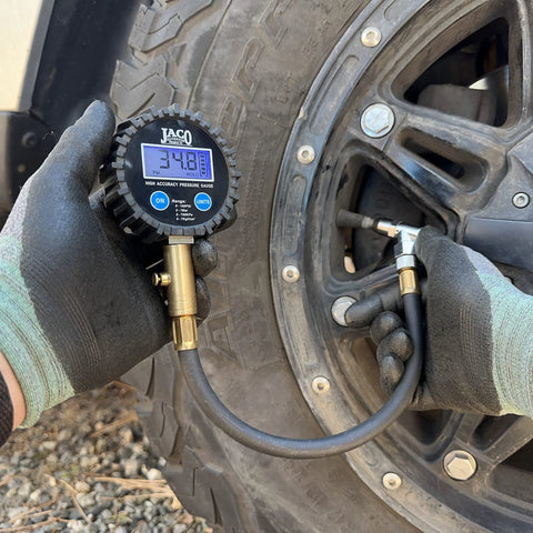 JACO ElitePro digital tire pressure gauge with brass nozzle attached to an automotive tire valve in use