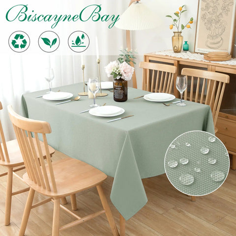 54x54 Inch Sage Square Tablecloth, Linen Like, Water Resistant And Washable, Ideal For Kitchen Dining, Picnics, Patio And Outdoor Parties, Restaurant Tables, Fits 24x24 To 42x42 Inch Square Tables, shown on a dining table with chairs and dishware