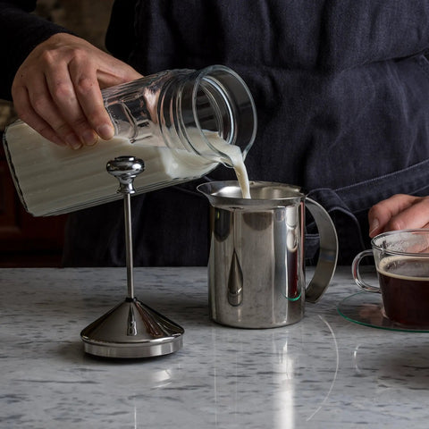 Person pouring milk into stainless steel handheld milk frother for creamy foam in seconds, 14 oz capacity.