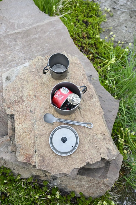 Ultralight Titanium Long Spoon For Backpacking And Camping beside cooking pot on rock, durable camp utensil with carabiner loop