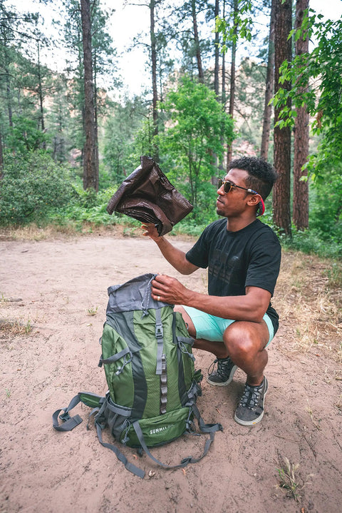 Man holding Rip Stop Tarp 8 By 10 Feet Heavy Duty Waterproof Brown Outdoor Shelter near green backpack in wooded area