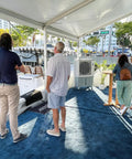 Image showing a gathering by a swamp cooler at an outdoor event, demonstrating its cooling power for guests.