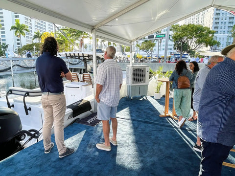 Image showing a gathering by a swamp cooler at an outdoor event, demonstrating its cooling power for guests.