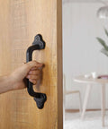 Hand using Rustic 9 Inch Cast Iron Sliding Barn Door Handle Set for indoor outdoor use, black finish, installed on wooden door