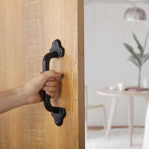 Hand using Rustic 9 Inch Cast Iron Sliding Barn Door Handle Set for indoor outdoor use, black finish, installed on wooden door