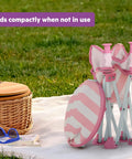 Folded Pop N Sit Cabana Baby Beach Portable Booster Chair with UPF Canopy next to picnic basket on grass