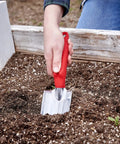 Heavy Duty Garden Trowel For Everyday Digging And Planting in raised bed with red handle and aluminum blade