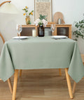 54x54 Inch Sage Square Tablecloth, Linen Like, Water Resistant and Washable on a dining table set for two with wine glasses