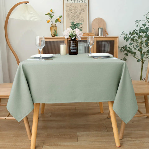 54x54 Inch Sage Square Tablecloth, Linen Like, Water Resistant and Washable on a dining table set for two with wine glasses