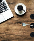 18 Pack Flexible Silicone Desk Cable Grommets With 1 Inch Hole Saw Heavy Duty Cord Hole Covers For Office Tables And Wall Panels Black on a wooden desk with a laptop and coffee.