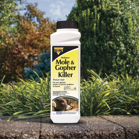One-pound Mole And Gopher Killer Poison Bait Granules bottle on patio with garden background for lawn pest control.