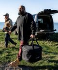 Man holding Venture Bag For Tread Pizza Oven And Roof Rack, Rugged Nylon Carry Case with reinforced top, near parked SUV.