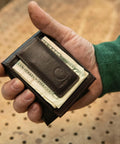 Premium Full Grain Leather Slim Bifold Wallet For Men In Rich Oil Tan Brown held in a hand with cash, showcasing its lightweight design.