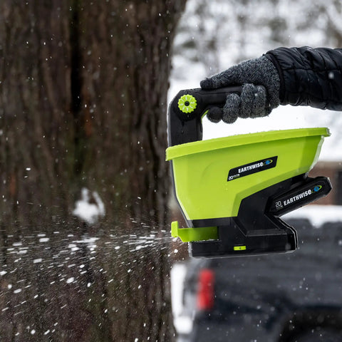 20-Volt Cordless Handheld Seed And Fertilizer Spreader For Yard Work in snow, gloved hand adjusting spreading rate dial