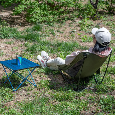 Person sitting on ultralight low profile camping folding chair with side pocket and carry bag 7.5 inch seat height ultra compact and stable on uneven ground