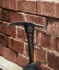 IsoCore Pickaxe Mattock With Shock Absorbing Handle prying bricks on a wall, showing dual head for tough ground break up.