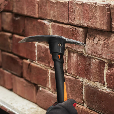 IsoCore Pickaxe Mattock With Shock Absorbing Handle prying bricks on a wall, showing dual head for tough ground break up.