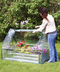 Woman opening mini greenhouse on Steel Raised Garden Bed With Mini Greenhouse Cover For Outdoor Growing, 4x3 foot size