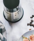 Portable Electric Coffee Grinder With Stainless Steel Burrs And Nine Precision Settings For Espresso To French Press Compact Grab And Go Design With No Sweat Cleanup For Top Shelf Daily Grinds Anywhere on a marble countertop with coffee beans.