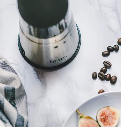 Portable Electric Coffee Grinder With Stainless Steel Burrs And Nine Precision Settings For Espresso To French Press Compact Grab And Go Design With No Sweat Cleanup For Top Shelf Daily Grinds Anywhere on a marble countertop with coffee beans.