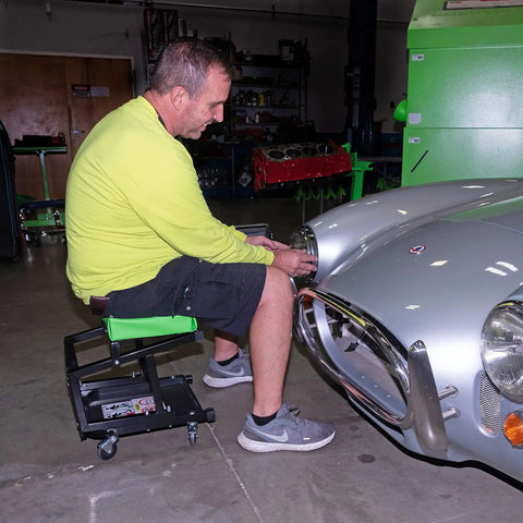 Man using 2 In 1 Mechanic Stool And Step Stool With Rolling Seat Adjustable Height Thick Padded Vinyl Cushion 300 lb Capacity Five Swivel Casters for auto repair.