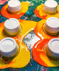 Colorful paint pouring over plastic cups demonstrating Floetrol Additive For Latex And Acrylic Paints To Improve Flow And Brushability
