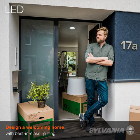 Man standing by open door with "LED" sign, surrounded by moving boxes and plant; promoting best-in-class home lighting.