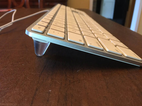 Side view of keyboard elevated by cone-shaped clear rubber bumper from 16 Piece Set Cone Shaped Clear Rubber Bumpers With Self Adhesive Tall Feet In 3 Sizes For Electronics, Computer Equipment, Audio Gear, Car Truck Accessories, Cutting Boards, Picture Frames, Cabinet Doors And More set.