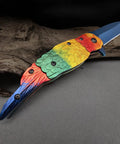 Colorful Parrot Pattern Folding Pocket Knife With Gradient Parrot-Scale Handle, 3-Inch Blue Coated Blade, 7.7 Inch Overall, Lightweight EDC Utility Knife For Camping, Outdoor Tasks, Daily Carry on rustic background
