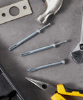 100 Pack One Quarter Inch By Three Inch Drive Nails For Anchor Hammer In Expansion Anchors Rustproof Zinc Plated Concrete Nails shown on a workbench with tools