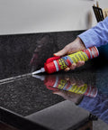 Hand applying Flex Caulk sealant from red-capped tube to black granite countertop seam.