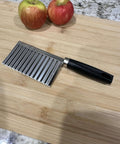Crinkle-cut wavy blade slicer with stainless steel blade and black handle on a wooden cutting board.