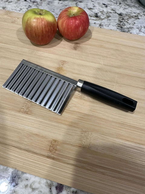 Crinkle-cut wavy blade slicer with stainless steel blade and black handle on a wooden cutting board.