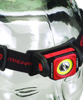 Twin Task 300-Lumen Headlamp With 3AA Batteries, red and black rubber strap, displayed on a glass head with adjustable elastic strap.