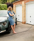 Woman standing near a parked electric vehicle with an EV Charger Protective Cover Heavy Duty Rust Proof Steel Shell Weatherproof Enclosure.