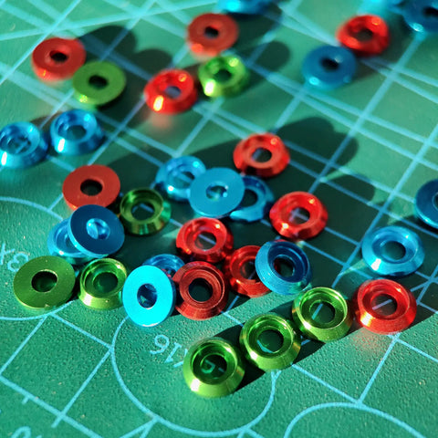 Colorful M3 counterbore washers in red, green, and blue anodized aluminum on a grid surface, perfect for RC Drone FPV use.