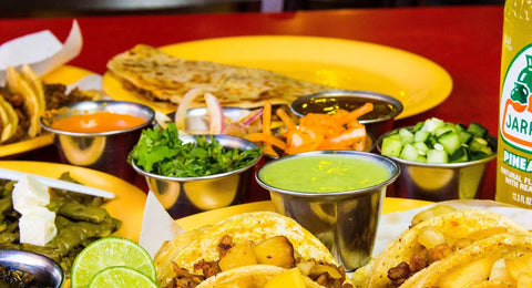Stainless Steel Sauce Cups Set 12-Pack Small Dipping Ramekins filled with condiments alongside tacos and lime slices on a table.