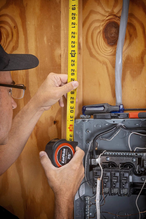 Person measuring wall with One And Three Sixteenths Inch By Sixteen Foot Tape Measure With Yellow Clad Command Control Anti Pinch Tip.